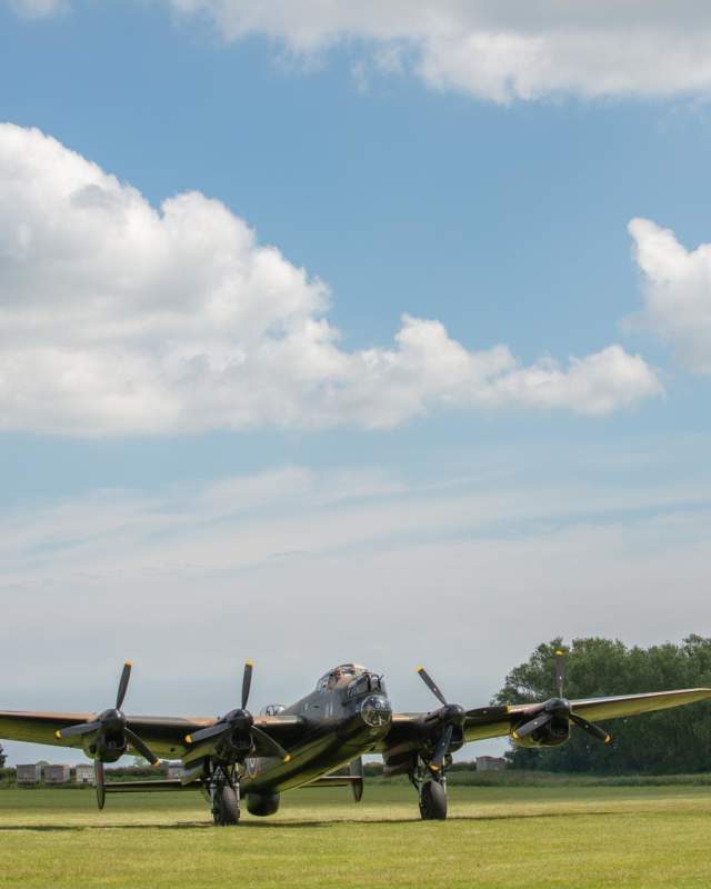 A Lancaster bomber plane on display on the ground with blue skies.