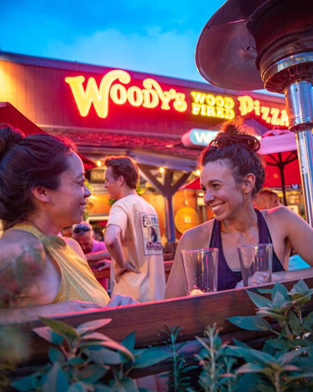 Two women drinking beer on outdoor patio at Woody's Pizza