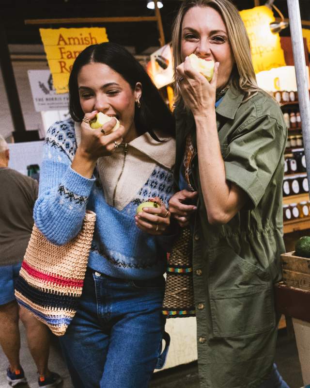 Two women eating apples in the middle of an indoor market