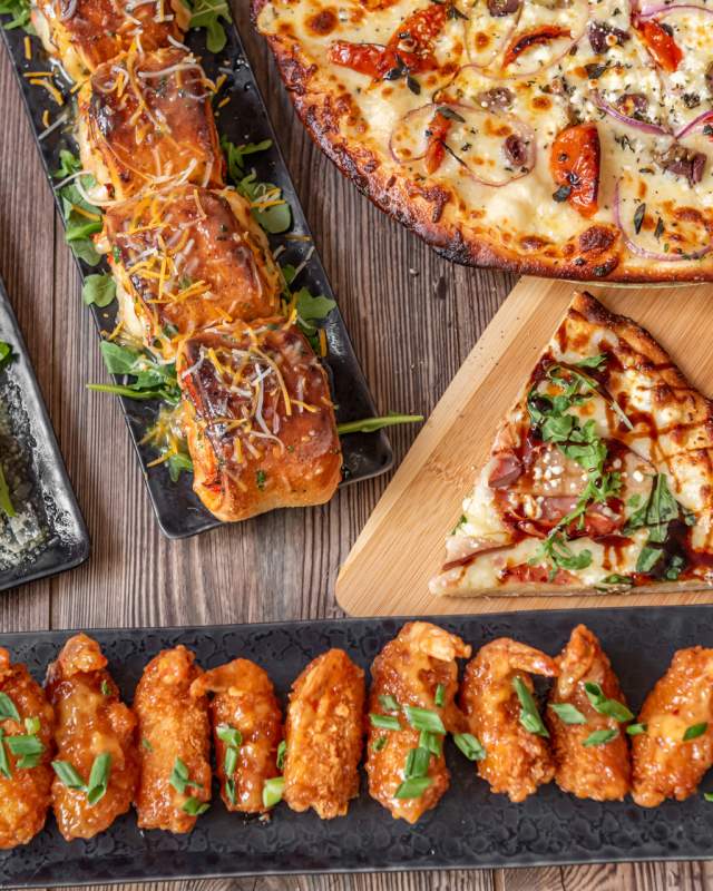 An image of chicken wings, pizza, pizza rolls, and other appetizers spread across a table showcasing the menu at doc & bubbas