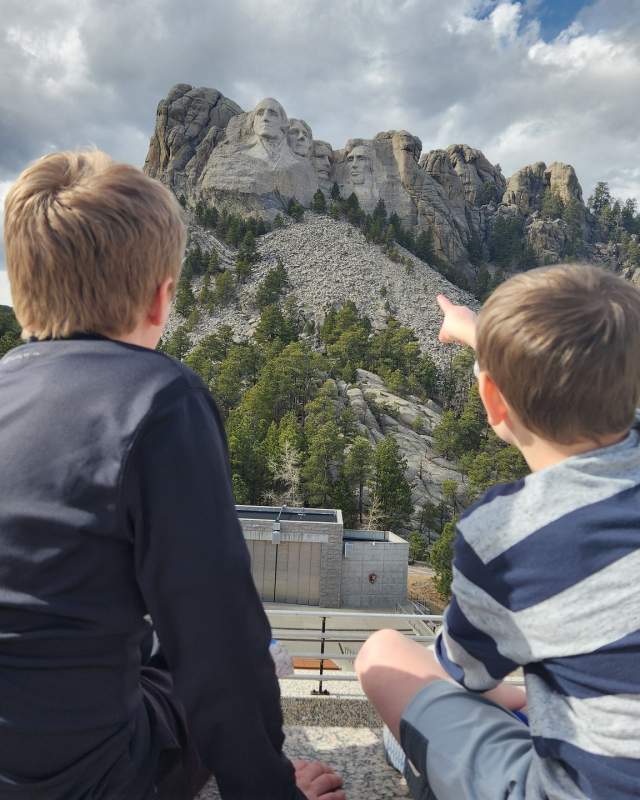 two kids sitting on the grand view terrace at mount rushmore pointing at the memorial