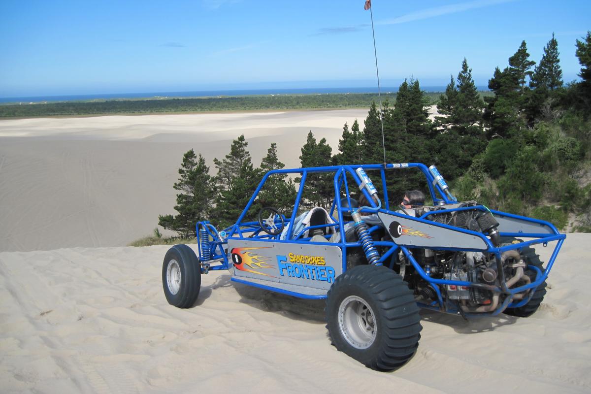 A dune buggy sits atop a large dune looking out towards the sea