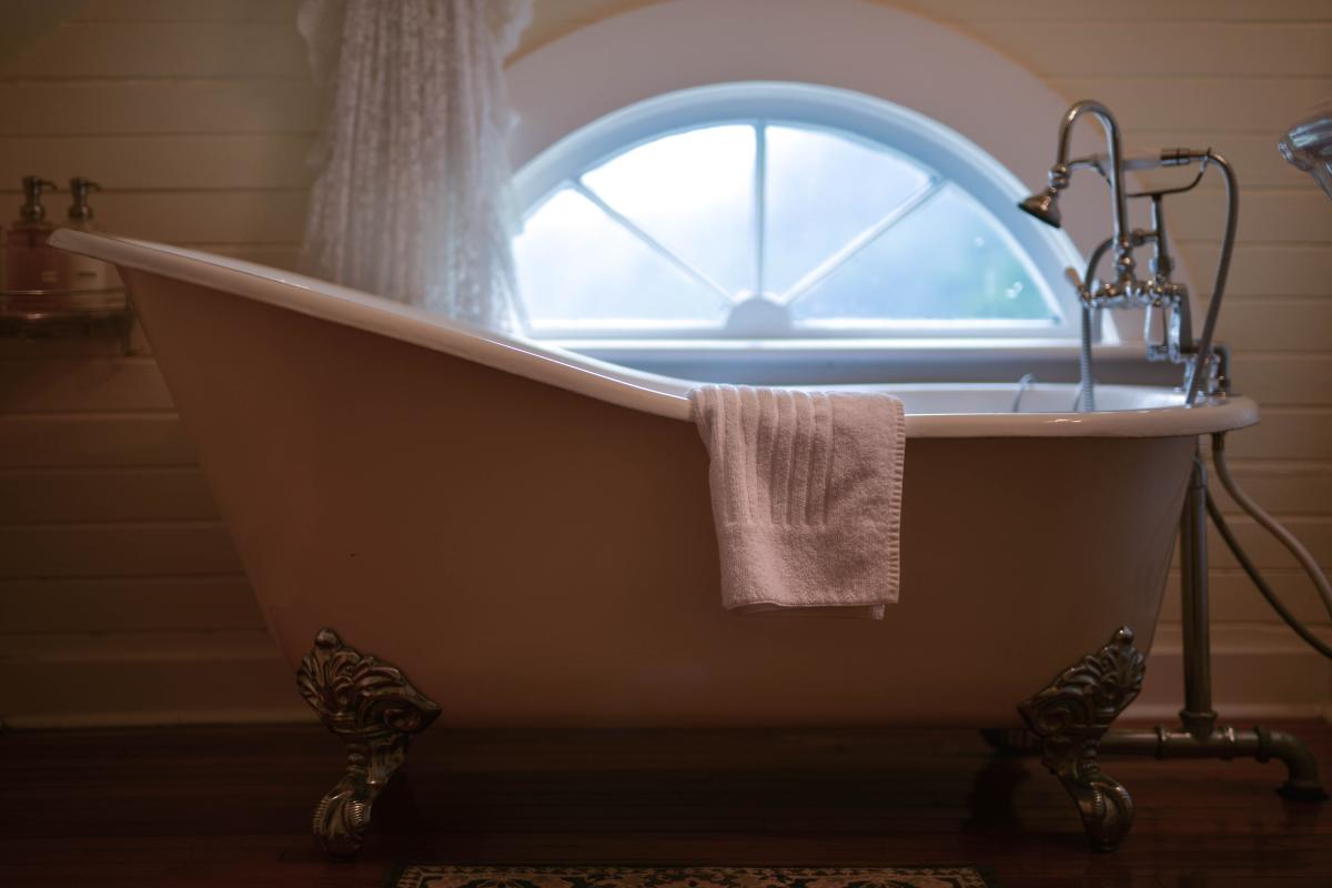 An antique claw foot tub with a white towel draped over the side sits in front of a small foggy window at the Heceta Head Lighthouse Bed & Breakfast.