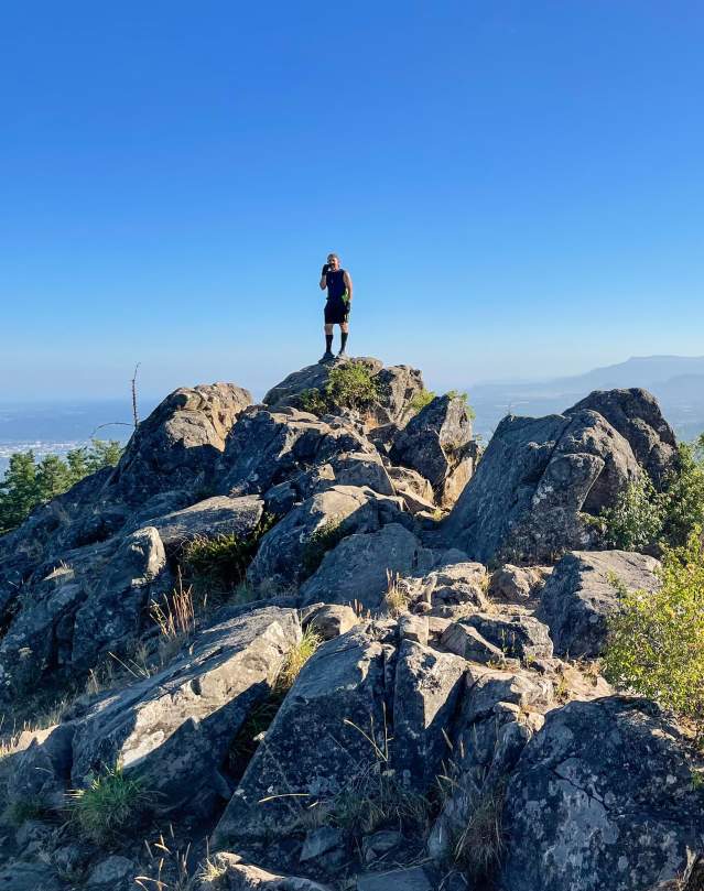 a man stands on top of a rocky summit with the valley down below.