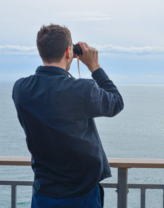 a man looks at the ocean with binoculars looking for whales.