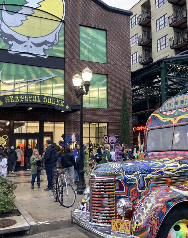 The colorful Further bus is parked in front of the Eugene Nike Store at Market Alley. A Grateful Dead yellow and green tribute is plastered across the building windows.