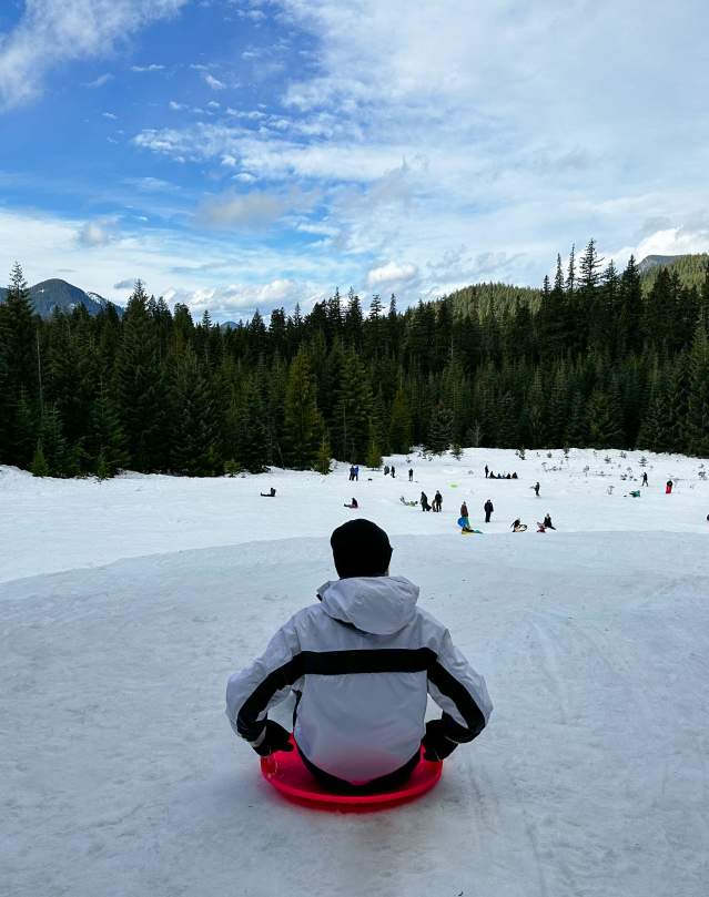 A person sits on a pink sled on top of a snow-covered hill.