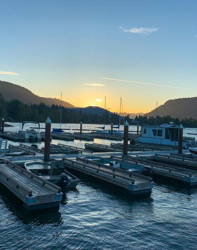 Docks on a lake with the sun rising over the mountains in the distance.