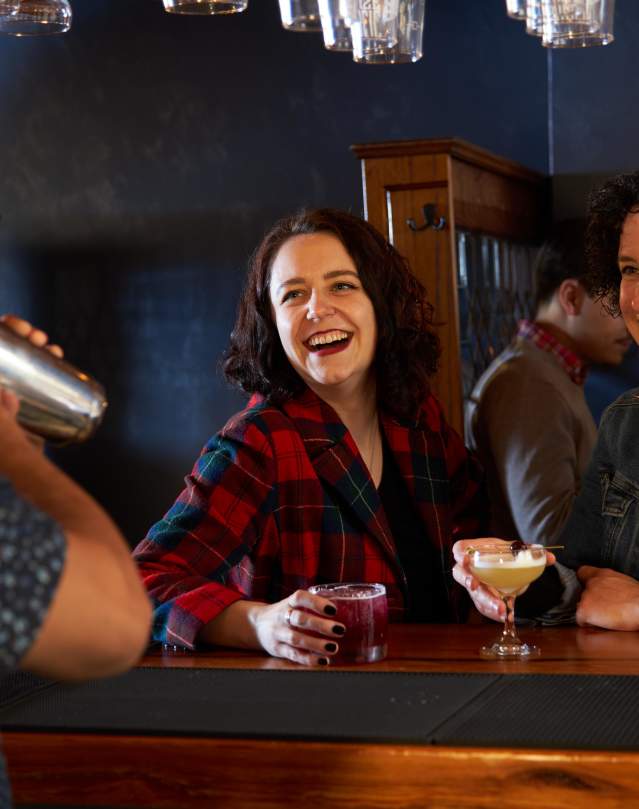 People sit at a bar with drinks, laughing with the bartender.