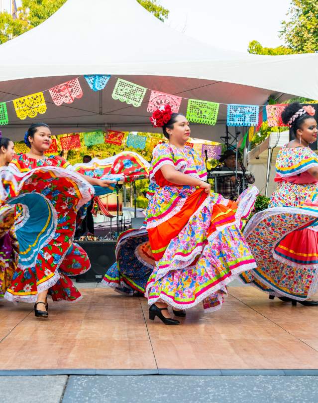 Dancers swirl brightly colored skirts as they dance on an outdoor stage.