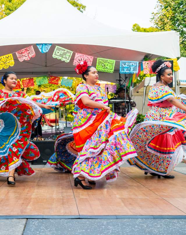 Dancers swirl brightly colored skirts as they dance on an outdoor stage.