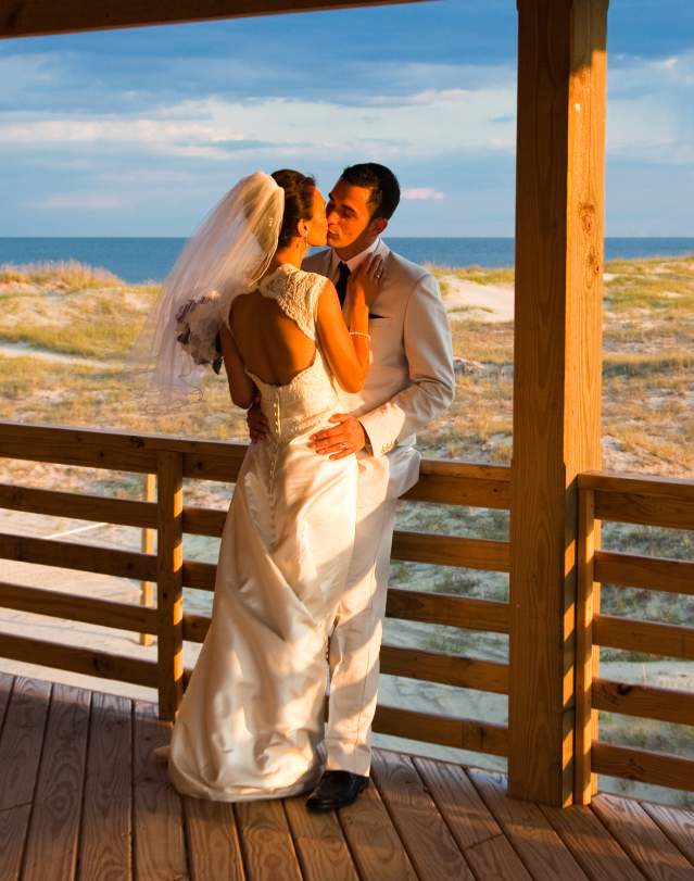 A couple on their wedding day kiss on a porch overlooking the beach in the Outer Banks