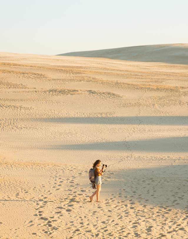 Woman walking in dunes and taking photos
