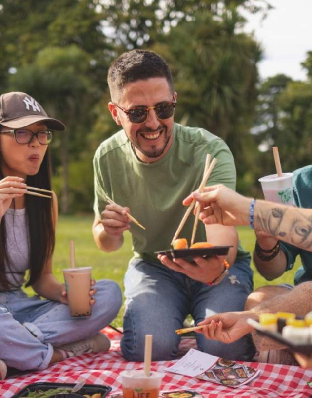 Group of friends enjoying sushi and bubble tea on a picnic blanket in the park