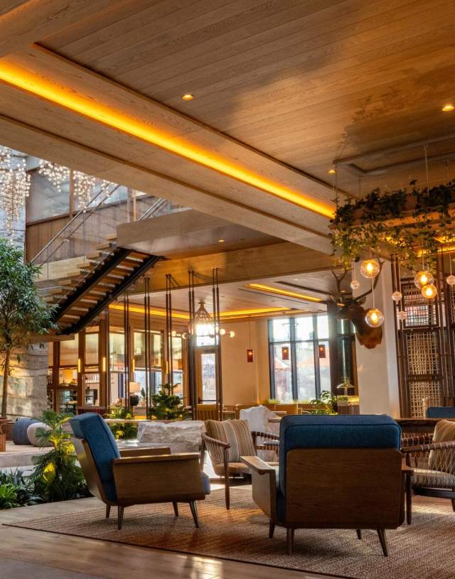 Modern lobby featuring natural stone walls, wooden beams, and stylish seating. Lush plants and warm lighting create a welcoming atmosphere.
