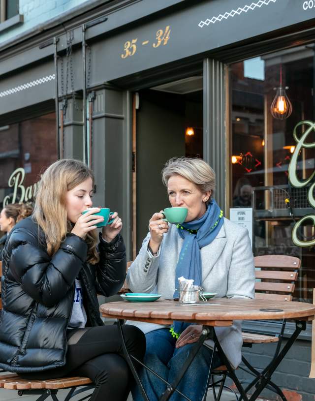 A mother and daughter enjoying coffee outside a cafe.