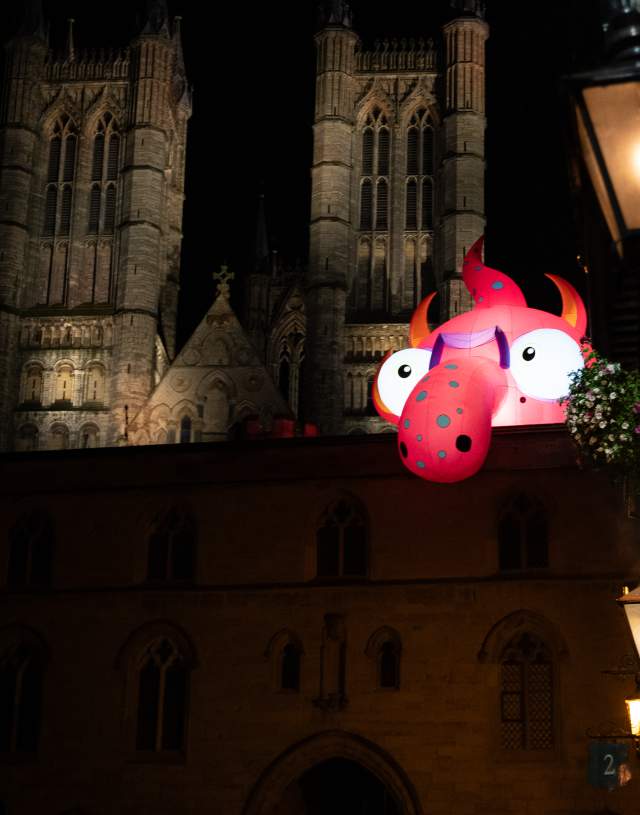 A red inflatable monster looking on from Lincoln Cathedral at night