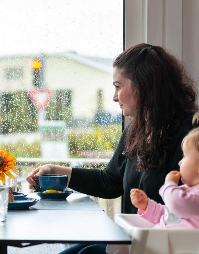 Mor og to barn sitter inne på kafé mens det regner utenfor