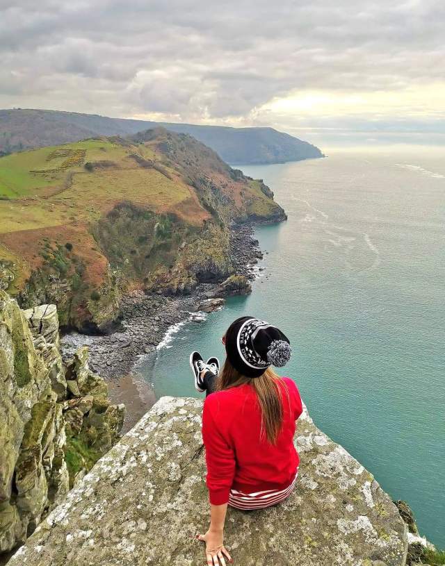 Lady sat on rock overlooking Valley of the Rock and the coast
