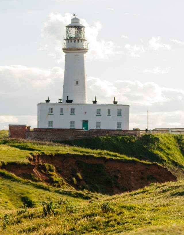 A couple walking part of the KCIII england coast path with the flamborough lighthouse in the background.