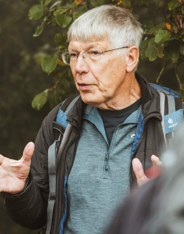 A focus on the tour guide of a walking group talking with the back of two people in view.