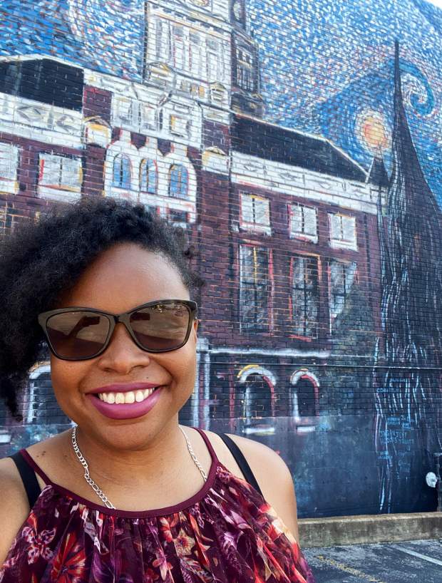 lady smiling in front of a large mural