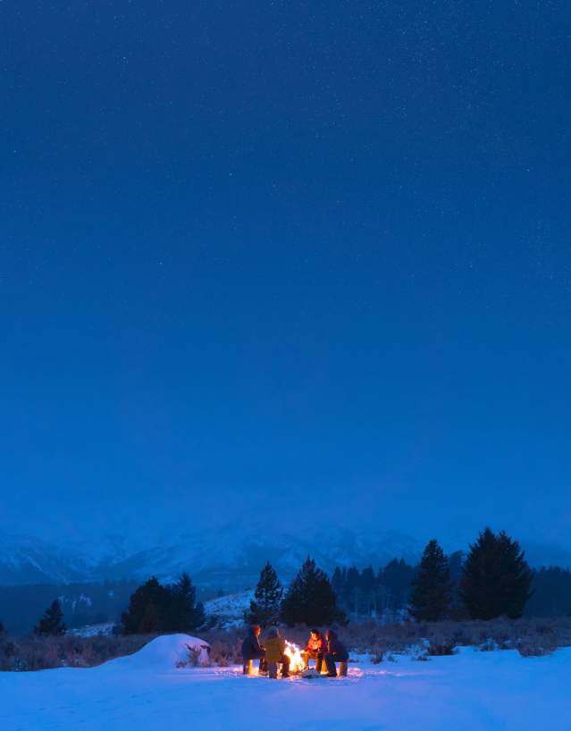 Group of people gathered around a campfire during winter.