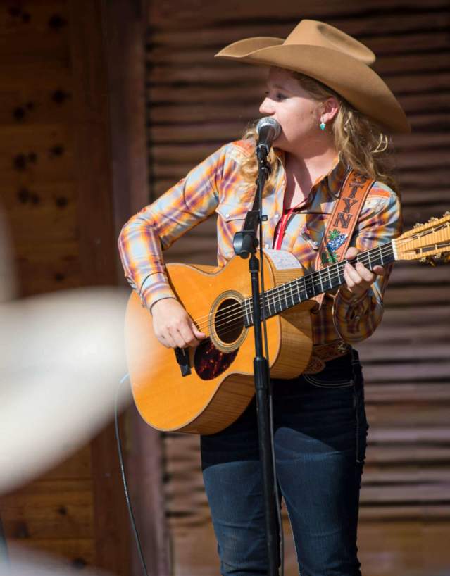 Performer with a guitar wearing a cowboy hat on stage.