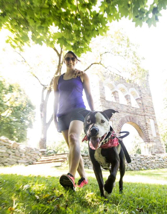 A woman and her dog hiking along the Appalachian Trail passing the War Correspondents Memorial Arch