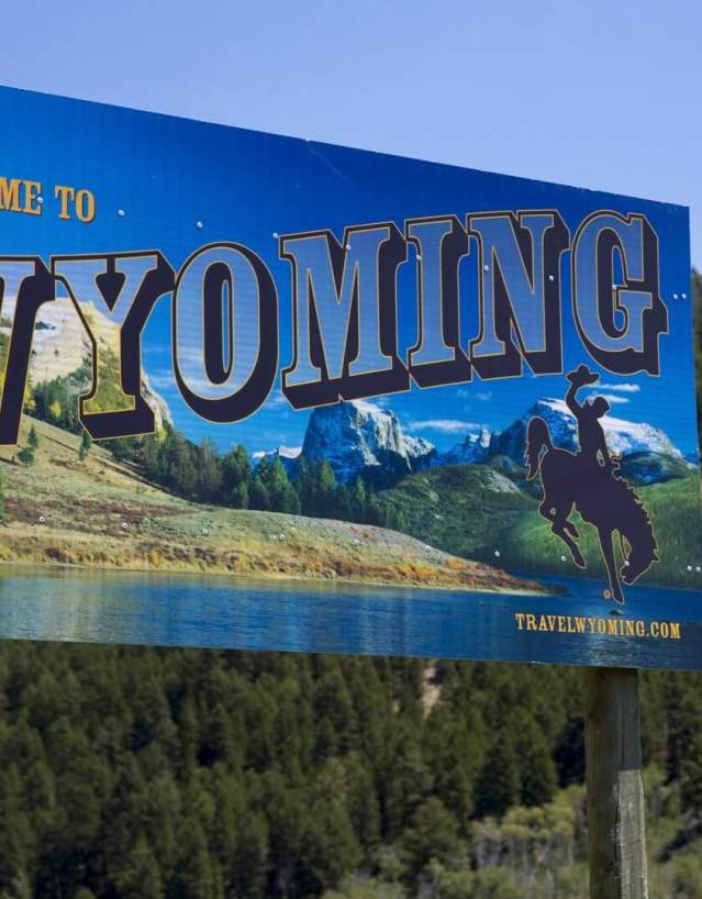 The Welcome to Wyoming road sign set against a forest covered mountain side.