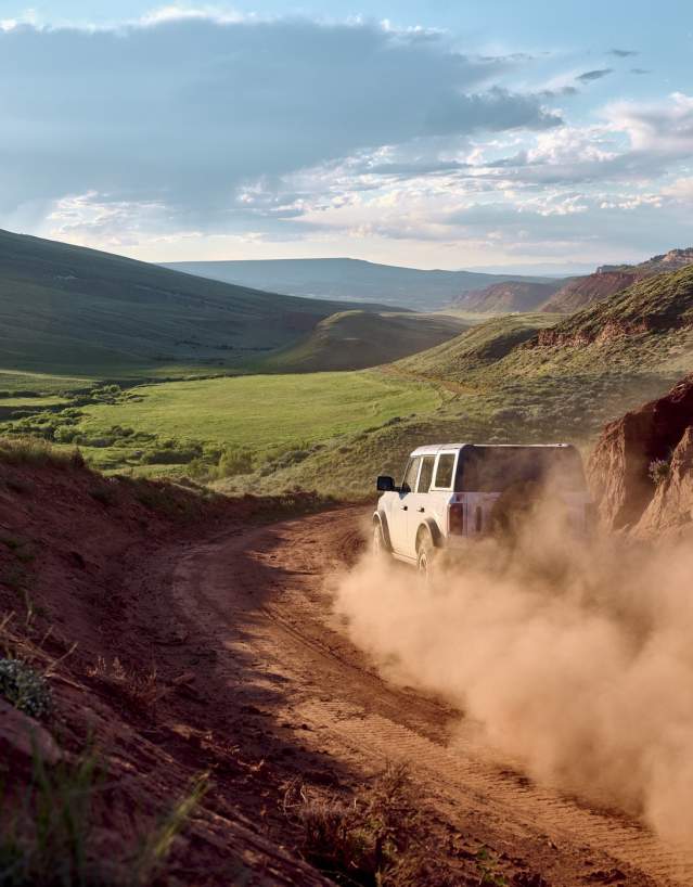 a dusty road with a vehcile driving along it through landscape