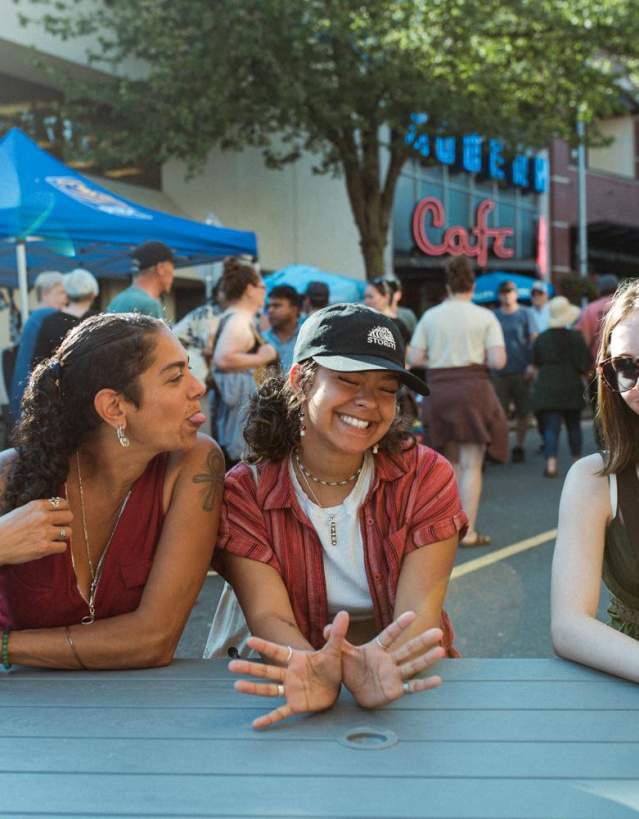 Three friends sitting at a picnic table teasing an goofing around with each other.