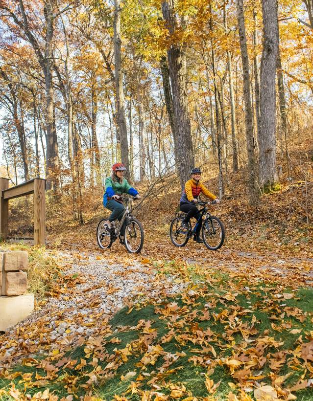 Mother and daughter mountain biking down a path in the fall