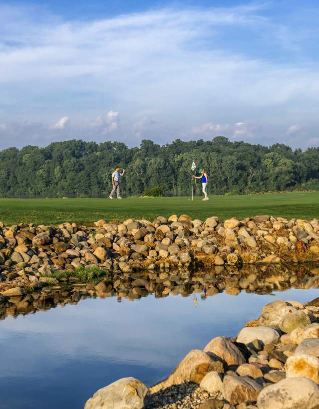 A couple on the putting green with rock wall and pond in the foreground