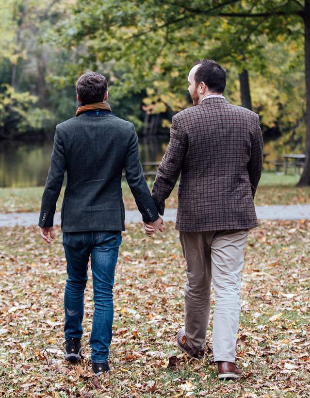 Two men holding hands in a park in the fall