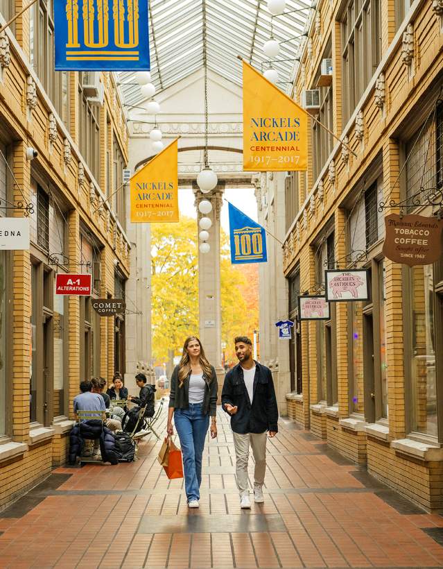 Couple walking in the center of a brick corridor with a glass roof, at Nickels Arcade