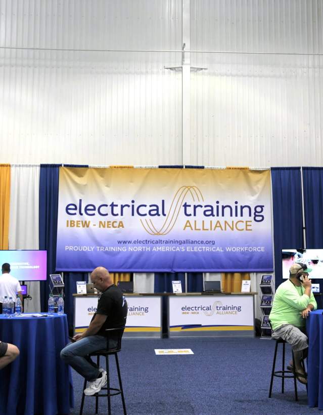 Men sitting at table in front of banner about electrical training