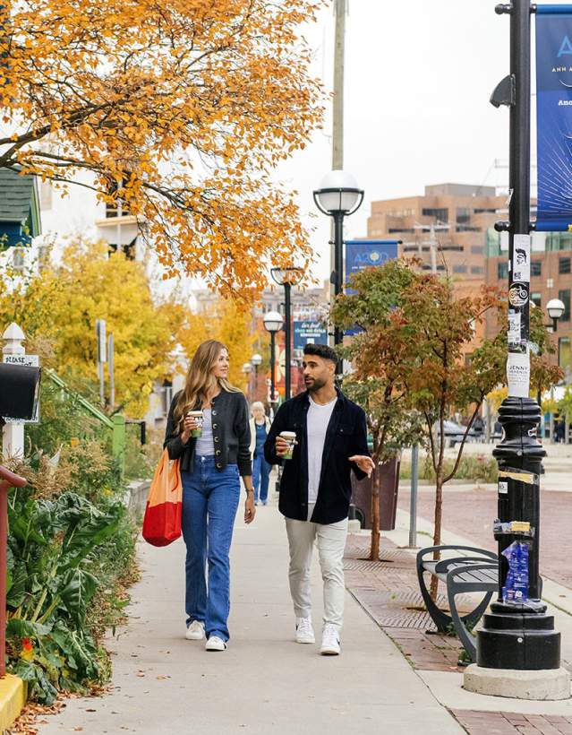 Man and woman holding coffee cups walk on sidewalk in front of Zingerman's Next Door Cafe