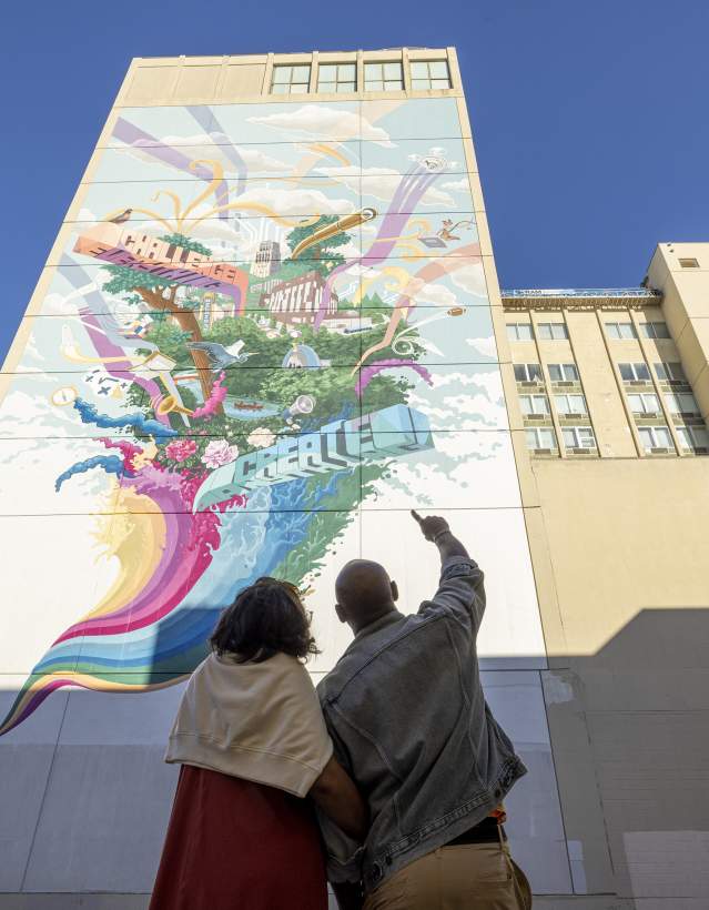 Couple pointing upward at tall, colorful mural