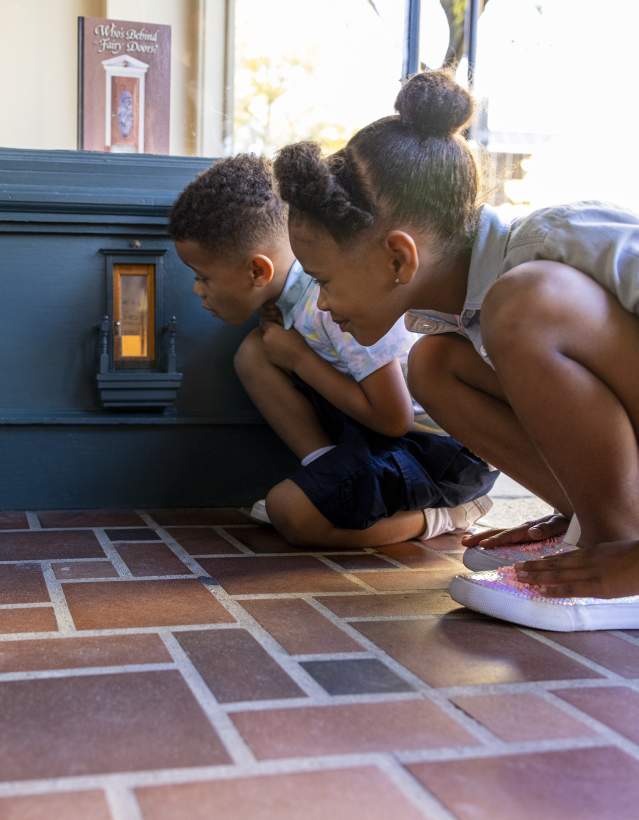 Two children kneeling down to look in a fairy door