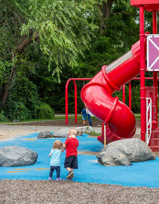 Two small children holding hands walking towards large red play structure