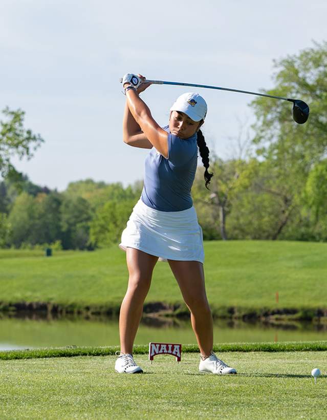 Girl teeing off with NAIA sign on grass