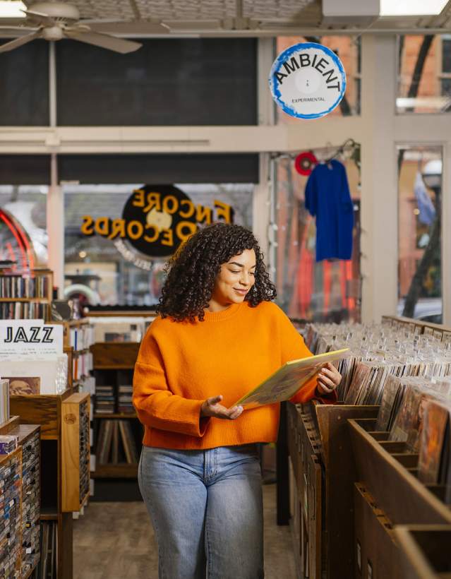 Encore Records- Woman in orange shirt looking at albums in a record store.