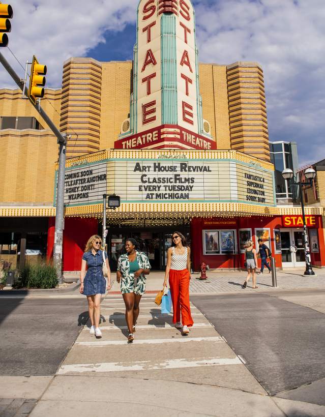 Three women walking across the crosswalk in front of the State Theatre