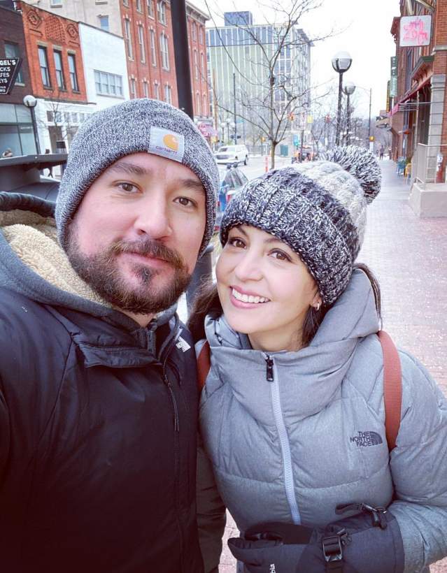 man and woman in winter coats and hats, smiling together on downtown street