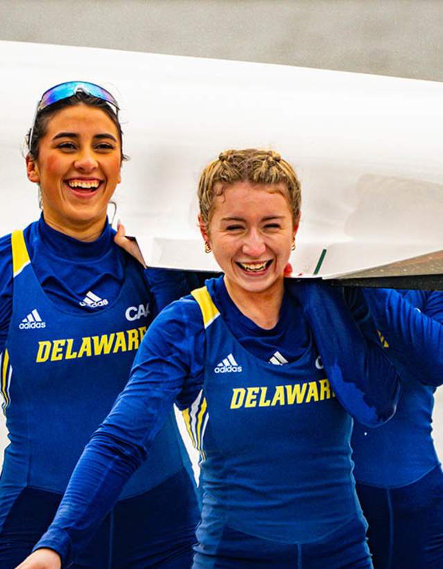 Female rowers carrying boat on shoulders and smiling