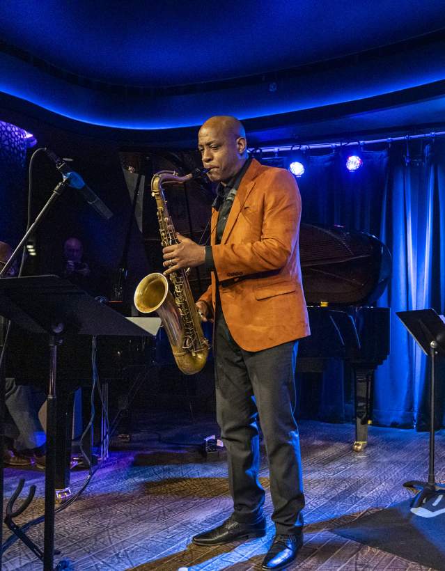 A man playing saxaphone and a woman playing stand up bass in a jazz club lit with blue lights