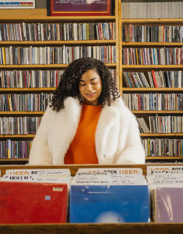 Encore Records- Woman in orange shirt and white jacket looking at albums in a record store.
