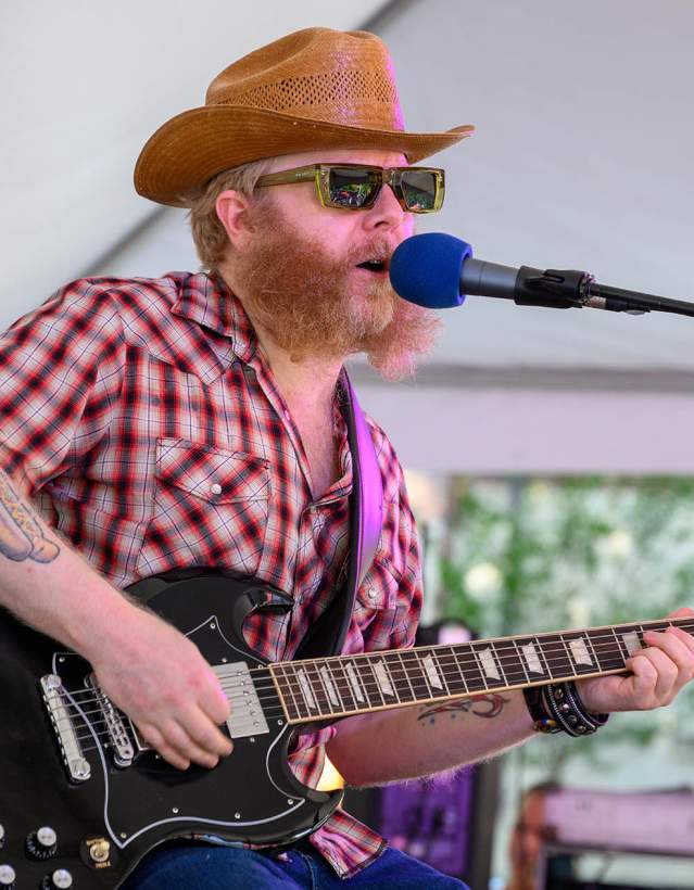 Man with hat, beard, and sunglasses playing guitar on stage