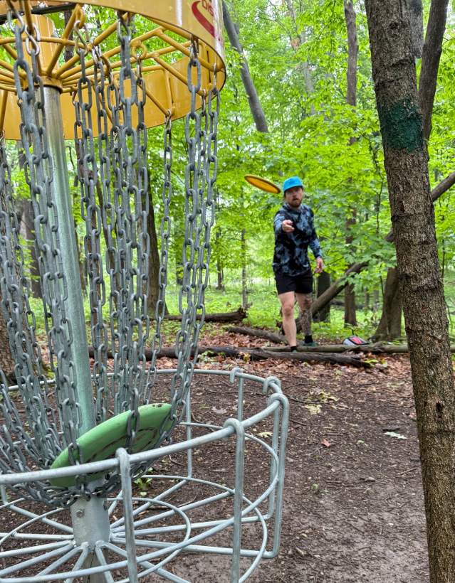Man disc golfs in heavily wooded area.